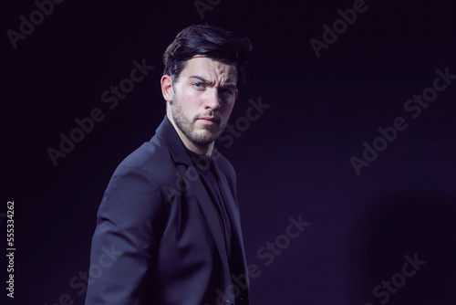 One Handsome Caucasian Brunet Businessman Wearing Black Suit Posing With Folded Hands Looking Aside Against Black