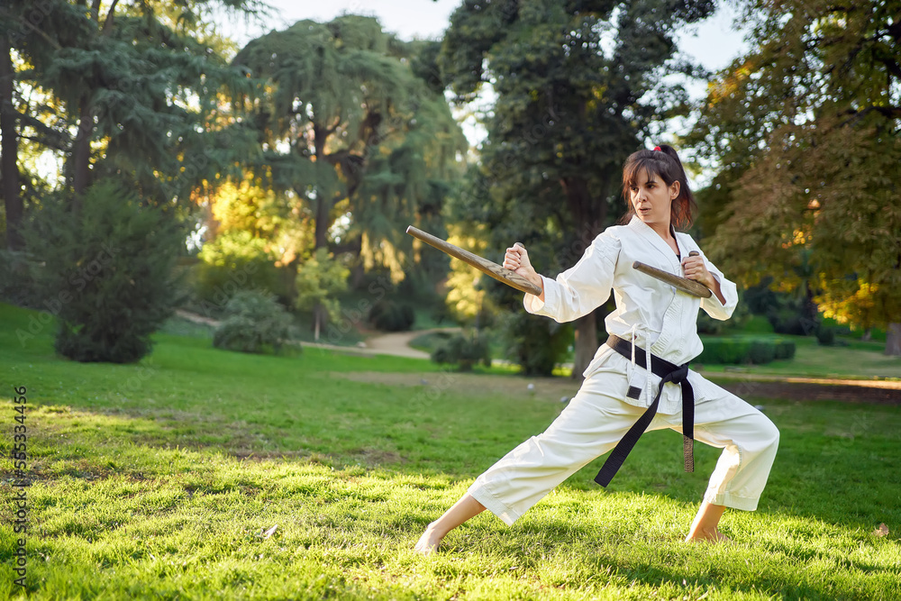 Karate fighter woman in white kimono and black belt in fighting stance outdoors in nature. Sports and martial arts concept.