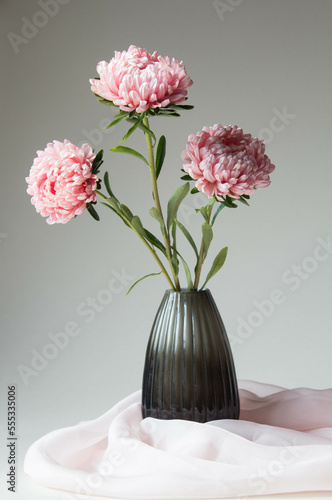 Bright pink flowers in a glass vase on  a neutral background. Elegant flower arrangement with silk scarf.