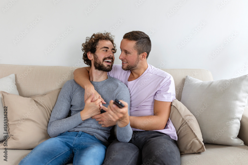 Young homosexual couple relaxing on sofa in the living room, embracing and enjoying while watching TV