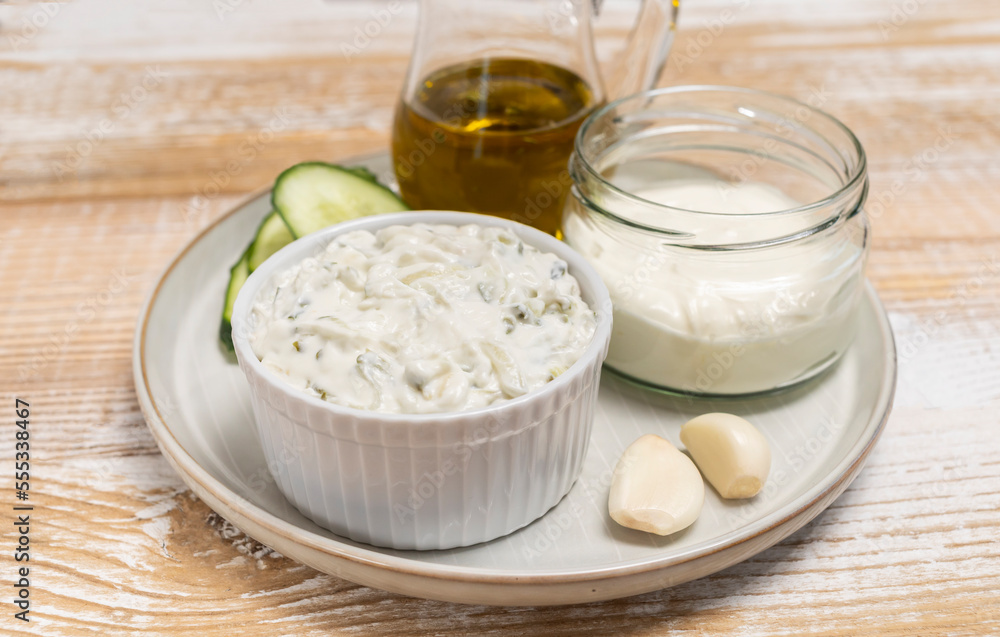 Traditional greek yogurt sauce Tzatziki,dressing in white bowl, made of grated cucumbers, sour cream yogurt,olive oil,garlic,herbs with ingredients on wooden table. Close up, horizontal Traditional greek yogurt sauce Tzatziki,dressing in white bowl, made of grated cucumbers, sour cream yogurt,olive oil,garlic,herbs with ingredients on wooden table. Close up, horizontal