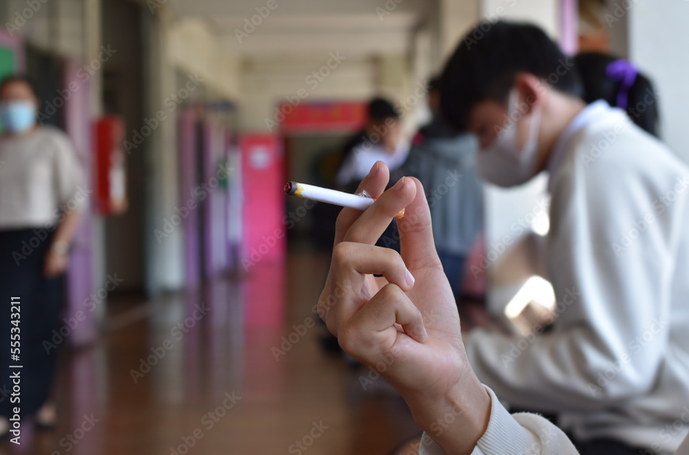 Closeup hand holding cigarette with blurred front balcony of classroom background, concept for smoking of asian young teenagers. Closeup hand holding cigarette with blurred front balcony of classroom background, concept for smoking of asian young teenagers.