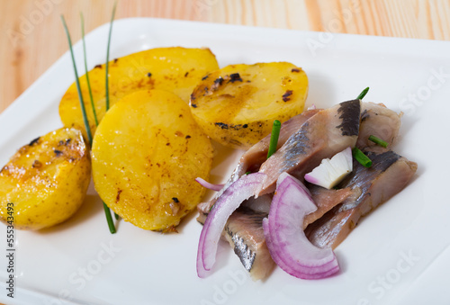 Slices of pickled herring with pieces of roasted potatoes and herbs served on plate photo