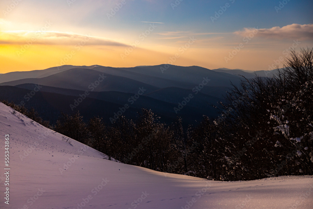 panorama of snow-capped mountains at sunset during a cold winter; mighty mountain peaks in the Polish Bieszczady mountains; mountain vegetation covered with snow