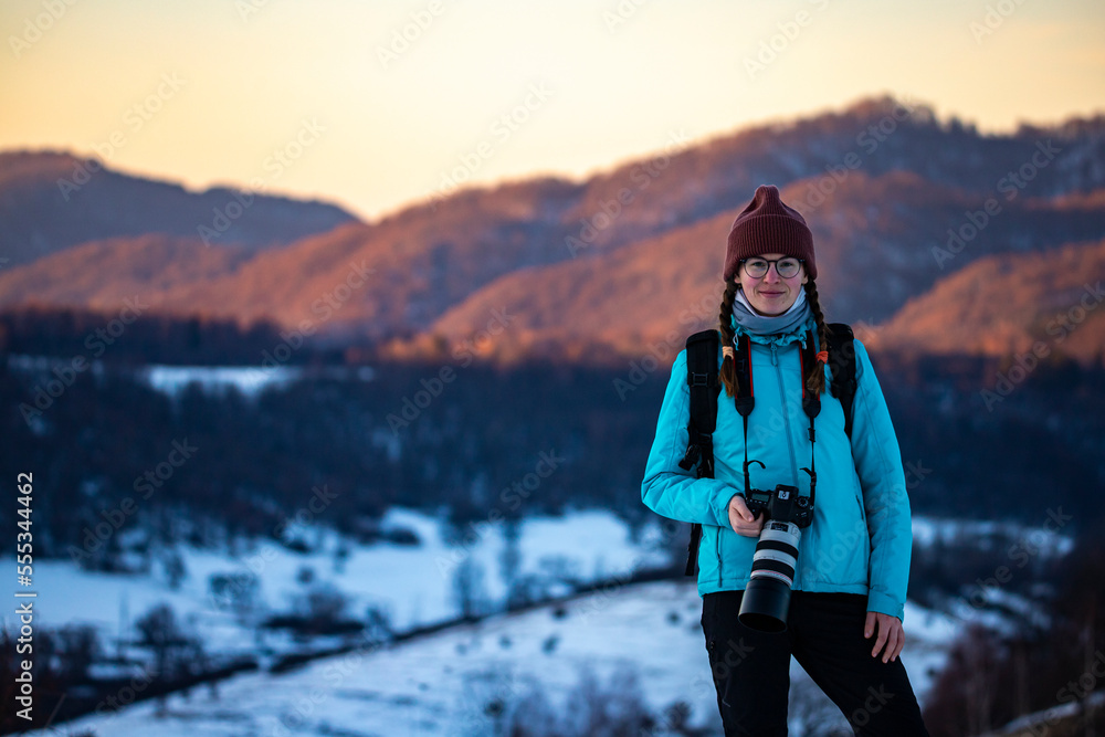 portrait of photographer woman during winter sunset, snowy hills in the background 