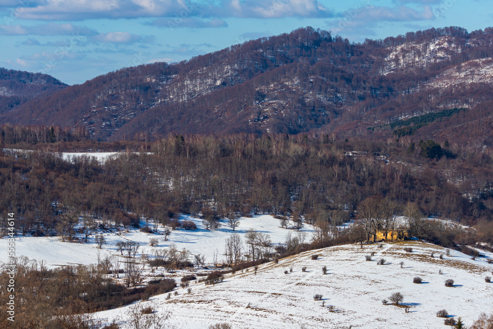 panorama of krywe village in polish bieszczady mountains by the san river; old destroyed orthodox church on the hill in snowy winter weather