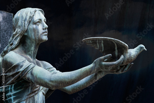 Statua, scultura. Ritratto, primo piano di donna ripreso in cimitero monumentale. La donna da il volo ad una colmba. Pace e serenutà. photo