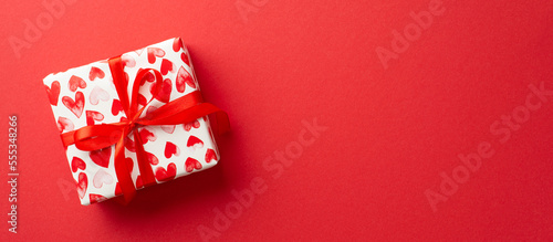 Valentine's Day concept. Top view photo of giftbox in wrapping paper with heart pattern on isolated red background with copyspace