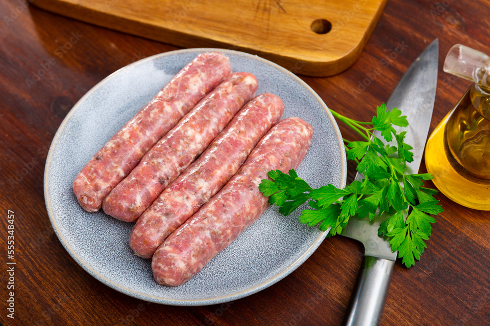 Raw white botifarra sausages from minced pork prepared for frying lying on plate with knife and fresh parsley. Traditional Catalan specialty