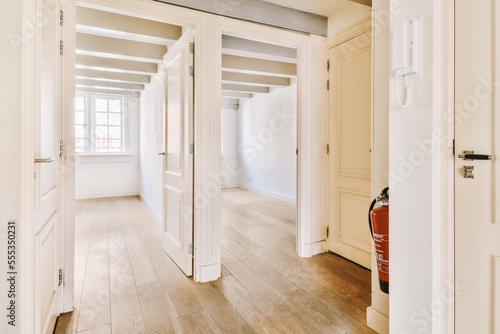 an empty room with white walls and wood flooring on the right side, there is a red fire exor in the door photo