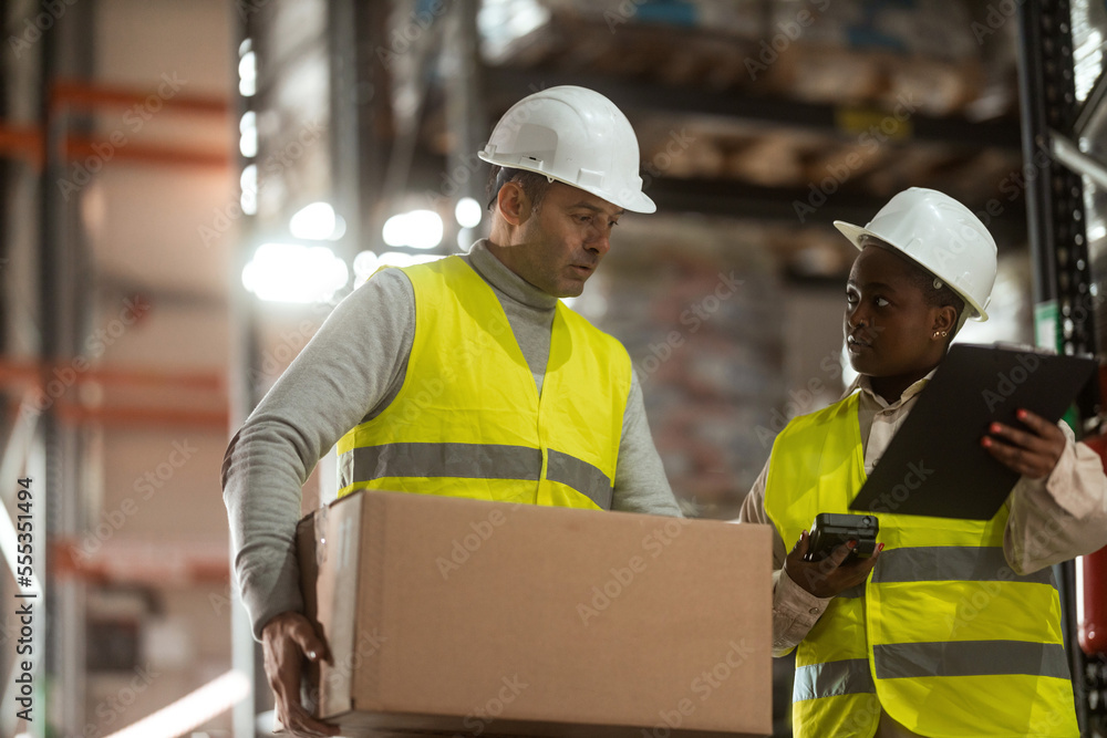 A shot of a man and woman working in a distribution warehouse, the manager is giving instructions to one worker. A shot of a man and woman working in a distribution warehouse, the manager is giving instructions to one worker.