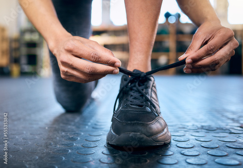 Tie, fitness or hands with shoes at gym for training, exercise or workout with motivation for a healthy lifestyle. Wellness, goals or sports athlete with foot wear ready to start exercising a club