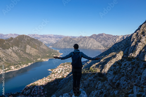 Hiking man with backpack with scenic view of Kotor bay at sunrise in summer, Adriatic Mediterranean Sea, Montenegro, Balkan, Europe. Fjord winding along coastal towns. Lovcen and Orjen mountain range