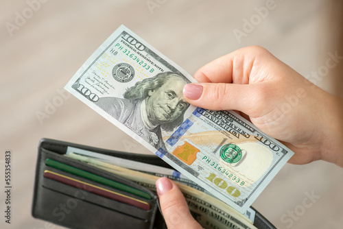 Paying for goods with dollar money, purchases and shopping. One hundred dollar banknote in female hands, wallet on the background
