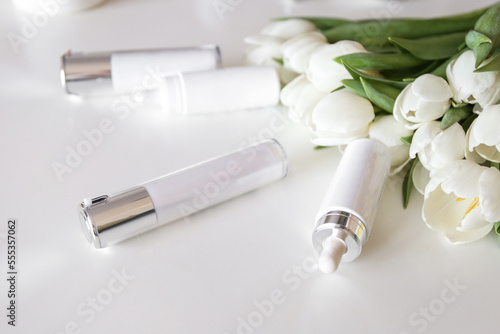 A set of professional cosmetics for the day on a white table near white tulips. Beauty rituals, youth, fight against wrinkles, acne, pigmentation, razacea.