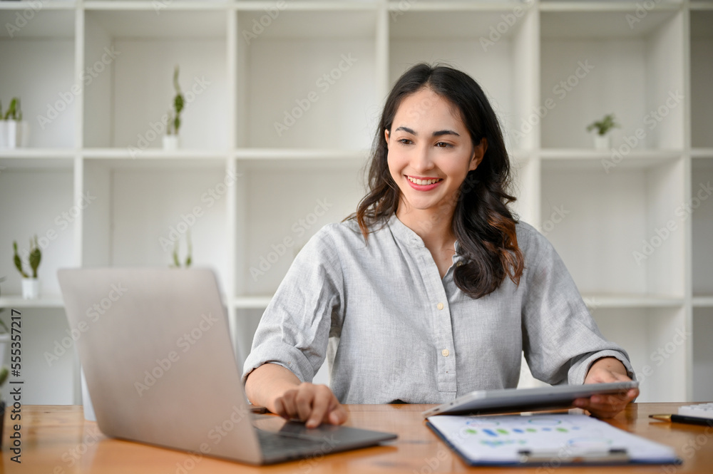 Gorgeous Asian businesswoman using laptop, reviewing business report, working at her desk Gorgeous Asian businesswoman using laptop, reviewing business report, working at her desk