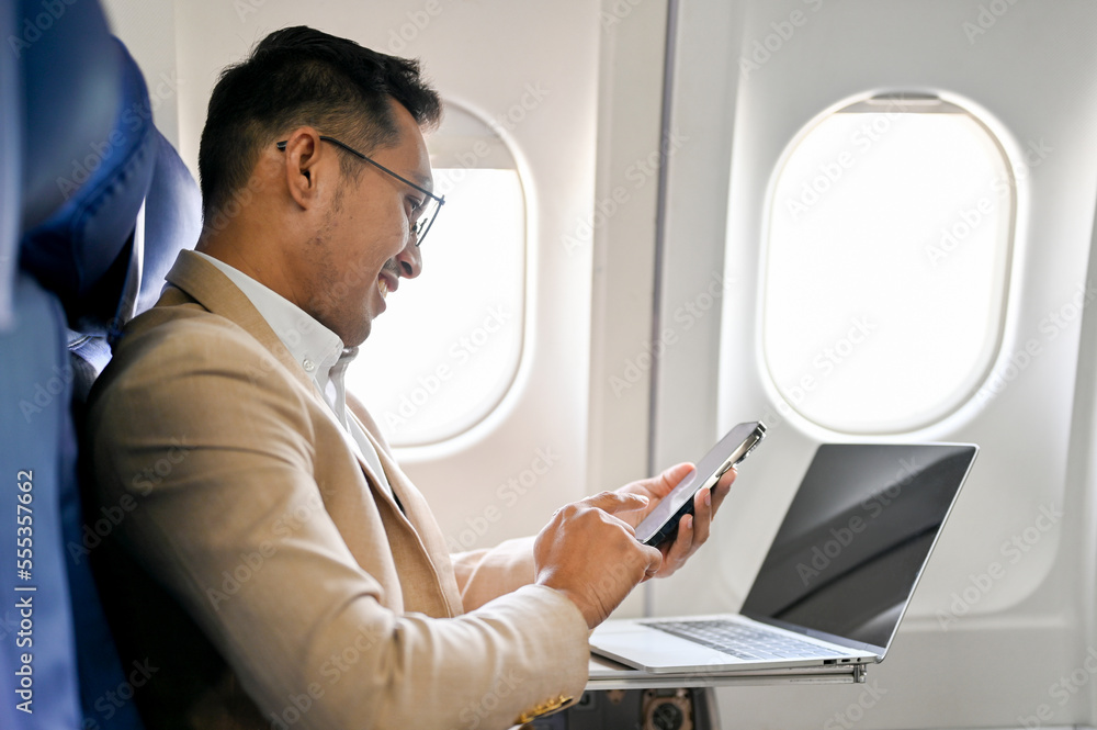side view, Smart Asian businessman sits at the window seat in business class using his smartphone side view, Smart Asian businessman sits at the window seat in business class using his smartphone