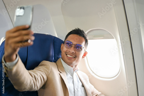 Successful Asian businessman taking his picture with smartphone during the flight