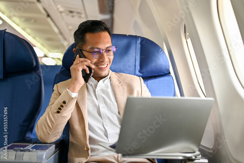Successful Asian businessman looks at his laptop screen, on the phone during the flight
