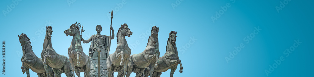 Banner with statue of Goddess Victoria with horses at the top of Triumphal Arch called Arch of Peace in Milan historical downtown, Sempione Park, Italy, at blue sky gradient background with copy space