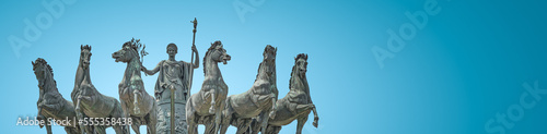 Banner with statue of Goddess Victoria with horses at the top of Triumphal Arch called Arch of Peace in Milan historical downtown  Sempione Park  Italy  at blue sky gradient background with copy space