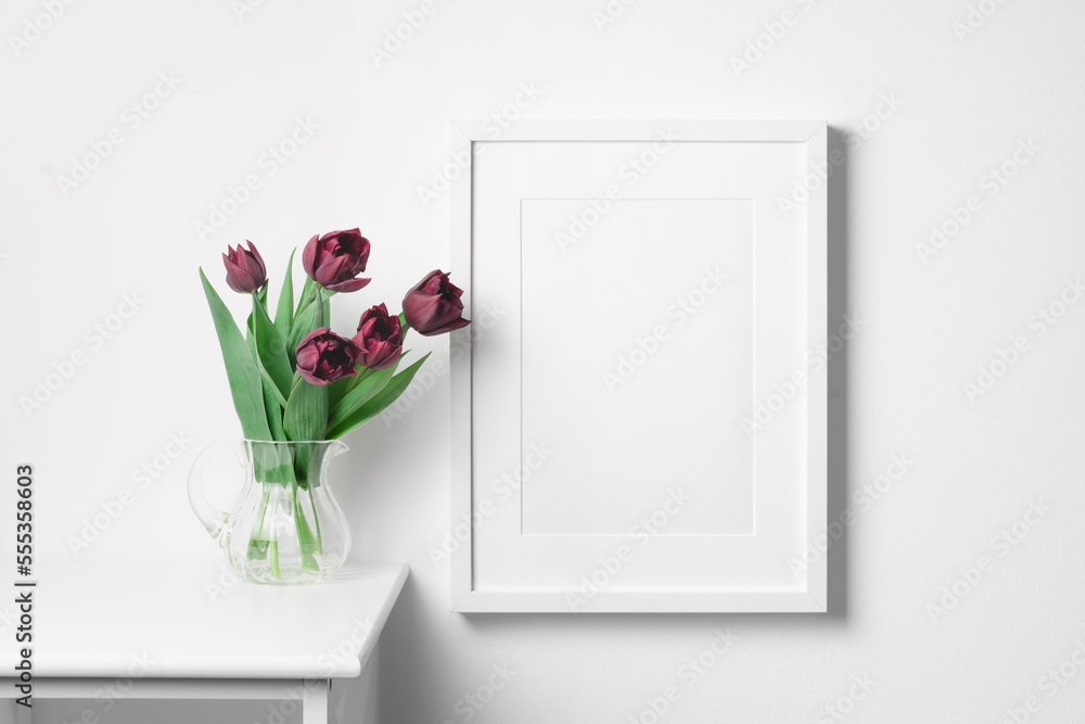 Blank portrait frame mockup on white wall with tulip flowers in vase Blank portrait frame mockup on white wall with tulip flowers in vase