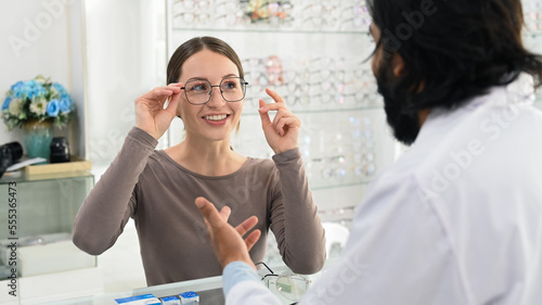 Smiling caucasian woman choosing spectacles glasses with professional optician. Eye health check and ophthalmology concept