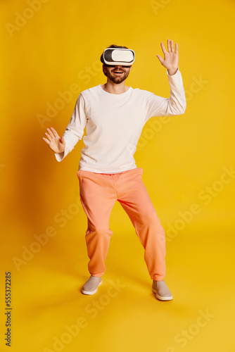Studio footage of young Caucasian man wearing casual style clothes using VR glasses isolated over yellow background. Emotions, games, technology, ad © Lustre Art Group 