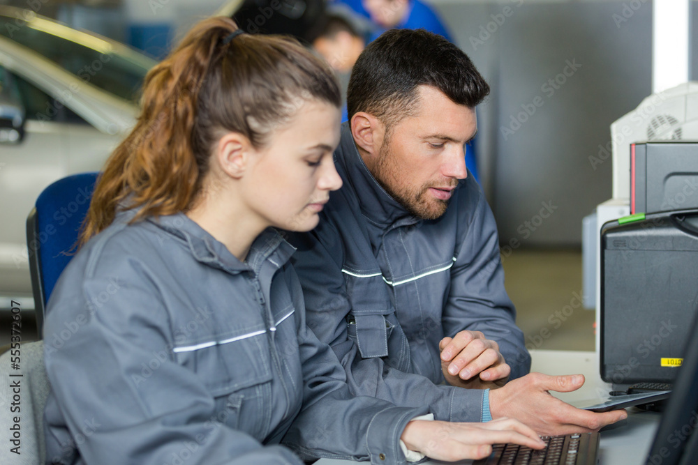mechanic and apprentice sat at computer desk looking at smartphone mechanic and apprentice sat at computer desk looking at smartphone