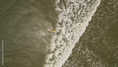Drone top down shot of surfer entering Atlantic ocean during sunny day with waves for surf lesson
