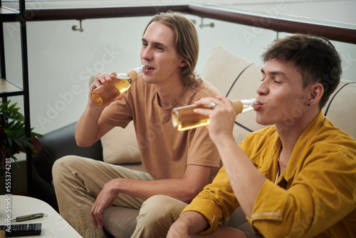 Young man drinking bottled beer when watching movie or soccer game at home