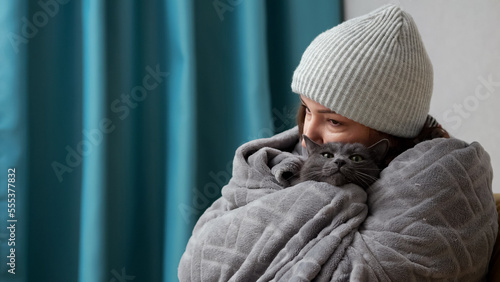 Canvastavla Woman wearing grey hat tries to warm herself and domestic cat with cosy blanket and hugs animal