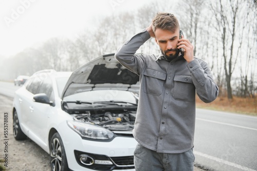Quadro su tela Man use a cellphone call garage in front of the open hood of a broken car on the road in the forest
