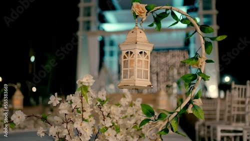 A beautiful vintage style white lantern hangs in an event garden at night with a canopy and lots of white chairs photo