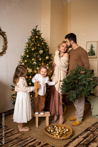 family, hygge and people concept - happy mother, father and little children near Christmas tree at home