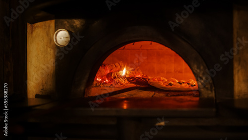 In Restaurant Professional Chef Uses Pizza Peel to Turn Pizza in the Wood Fire Stone Oven. Traditional Italian Cooking Family Recipe. Authentic Pizzeria, Delicious Organic Food. Front View No People