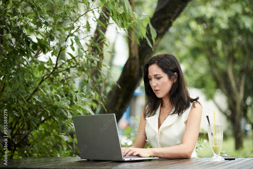 Elegant successful businesswoman sitting at table outdoors and working on laptop Elegant successful businesswoman sitting at table outdoors and working on laptop