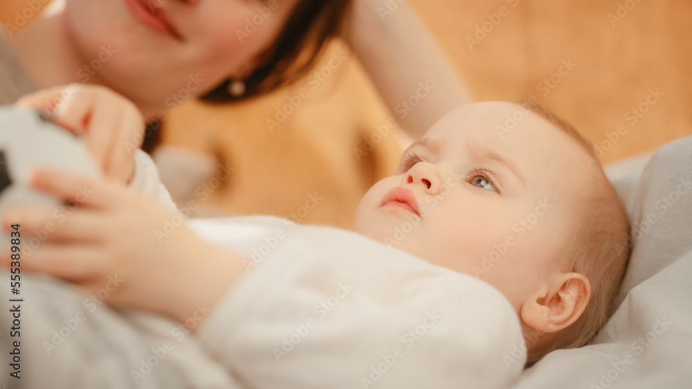 Caring Mother Lying on a Bed, Playing with a Cute Newborn Baby at Home. Mom Bonding with a Toddler, Baby Holding a Soccer Ball. Concept of Childhood, New Life, Motherhood. Caring Mother Lying on a Bed, Playing with a Cute Newborn Baby at Home. Mom Bonding with a Toddler, Baby Holding a Soccer Ball. Concept of Childhood, New Life, Motherhood.