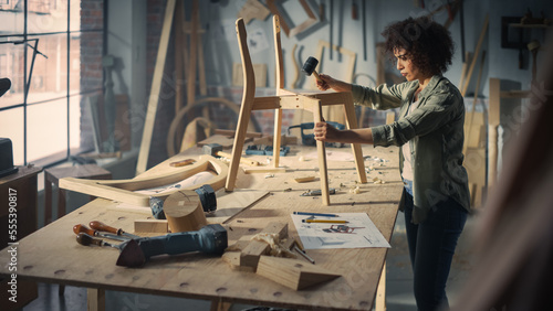 Young Stylish Female Carpenter Assembling a Wooden Chair. Professional Furniture Designer Working in a Studio in Loft Space with Tools on Walls Shot from an Angle Above. photo