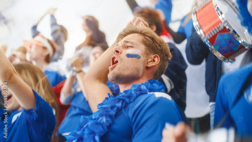 Sport Stadium Big Event: Handsome Happy Caucasian Man Emotionally Cheers, Screams. Crowd of Fans with Painted Faces Celebrate Championship Victor, their Blue Soccer Team is Winning. Sport Stadium Big Event: Handsome Happy Caucasian Man Emotionally Cheers, Screams. Crowd of Fans with Painted Faces Celebrate Championship Victor, their Blue Soccer Team is Winning.