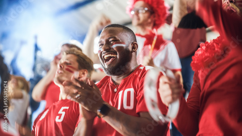 Sport Stadium Soccer Match: Diverse Crowd of Fans Cheer for their Red Team to Win. People Celebrate Scoring a Goal, Championship Victory. Group People with Painted Faces Cheer, Shout, Have Fun photo