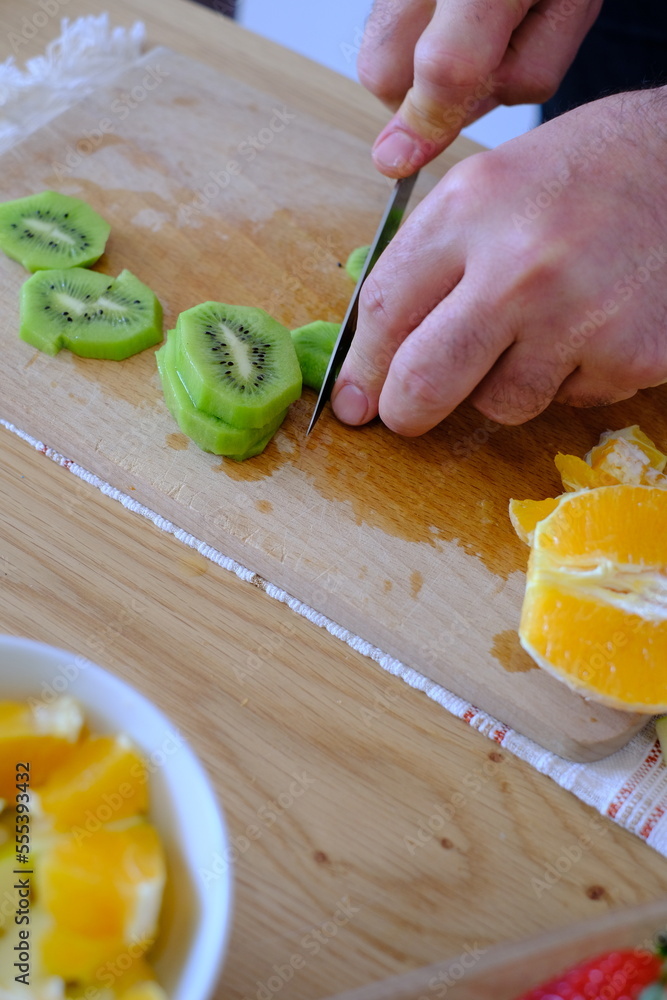 Man cutting kiwi on a wooden cutting board for fruit salad. Man cutting kiwi on a wooden cutting board for fruit salad.
