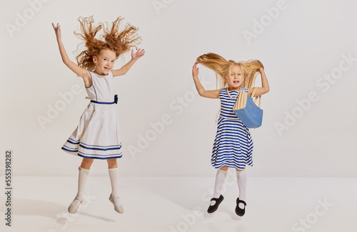 Portrait of two little girls, children in cute dresses posing, haing fun over grey background photo