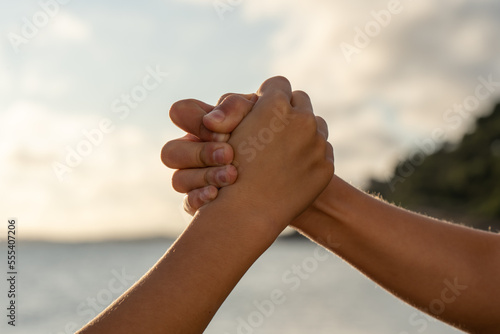 Anonymous boys clasping hands and supporting each other on blurred background of sea and cloudy sunset sky
