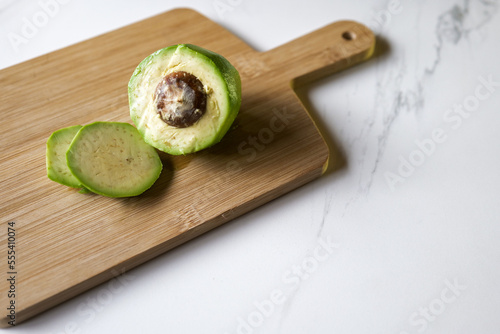 Peeled and cut avocado on wooden cutting board on marble kitchen top with toast in background