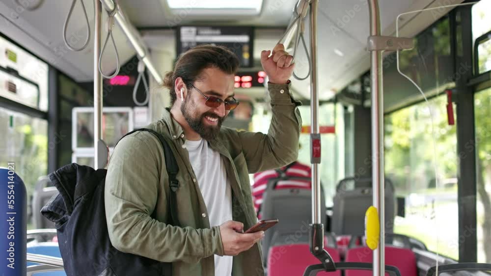 Side view of handsome man going by bus, standing, holding, using smartphone. Brunette male with earphones wearing sunglasses, texting, scrolling. Concept of public transport. Side view of handsome man going by bus, standing, holding, using smartphone. Brunette male with earphones wearing sunglasses, texting, scrolling. Concept of public transport.