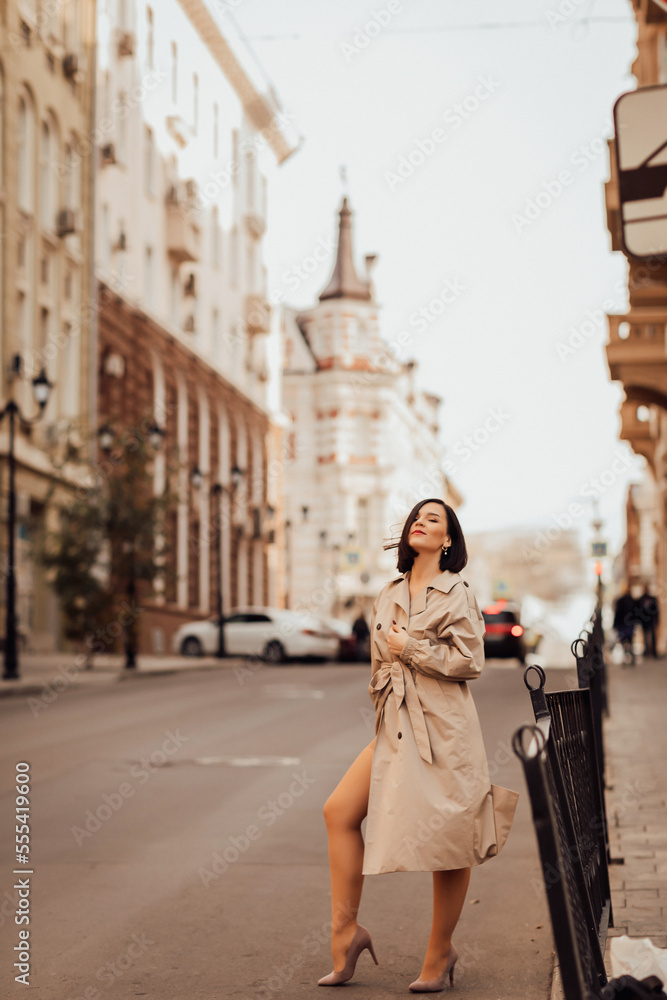 a beautiful brunette woman in a raincoat stops a car on the street of the city.