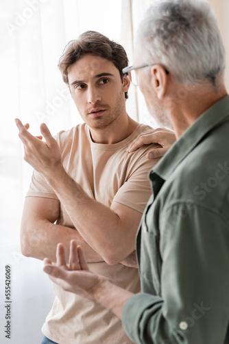mature man touching shoulder and talking to upset son on blurred foreground