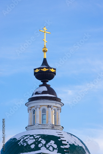 Green dome of the Orthodox Church with golden cross under snow against blue sky background