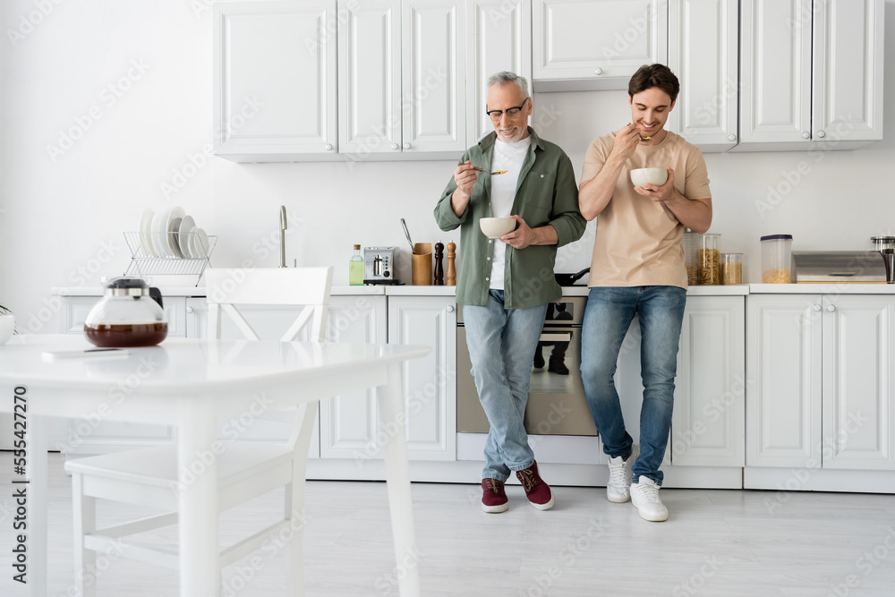 Obraz premium full length of mature father and young son having breakfast while standing in modern kitchen